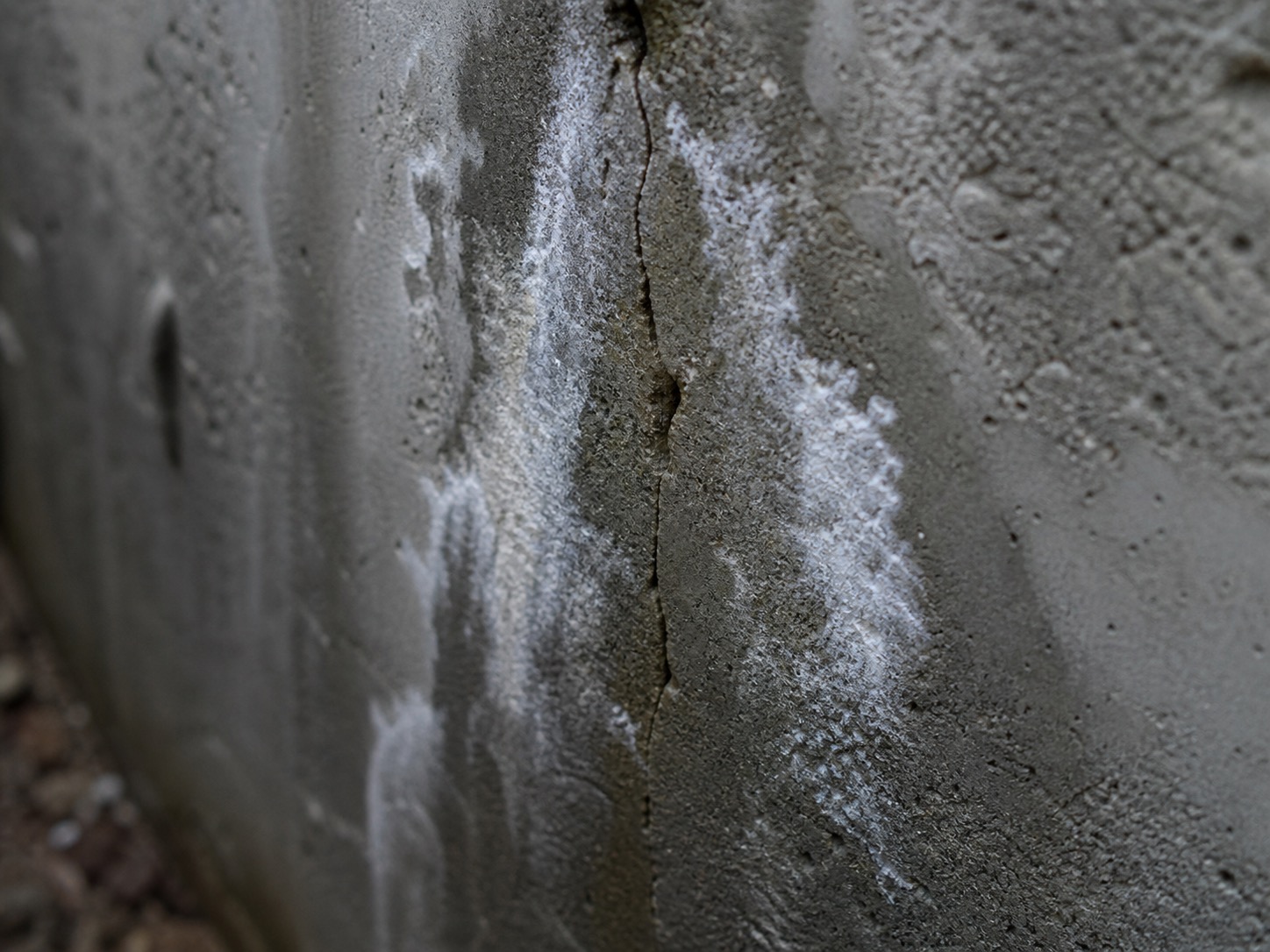 Fissure et efflorescence blanche sur un mur de fondation en béton
